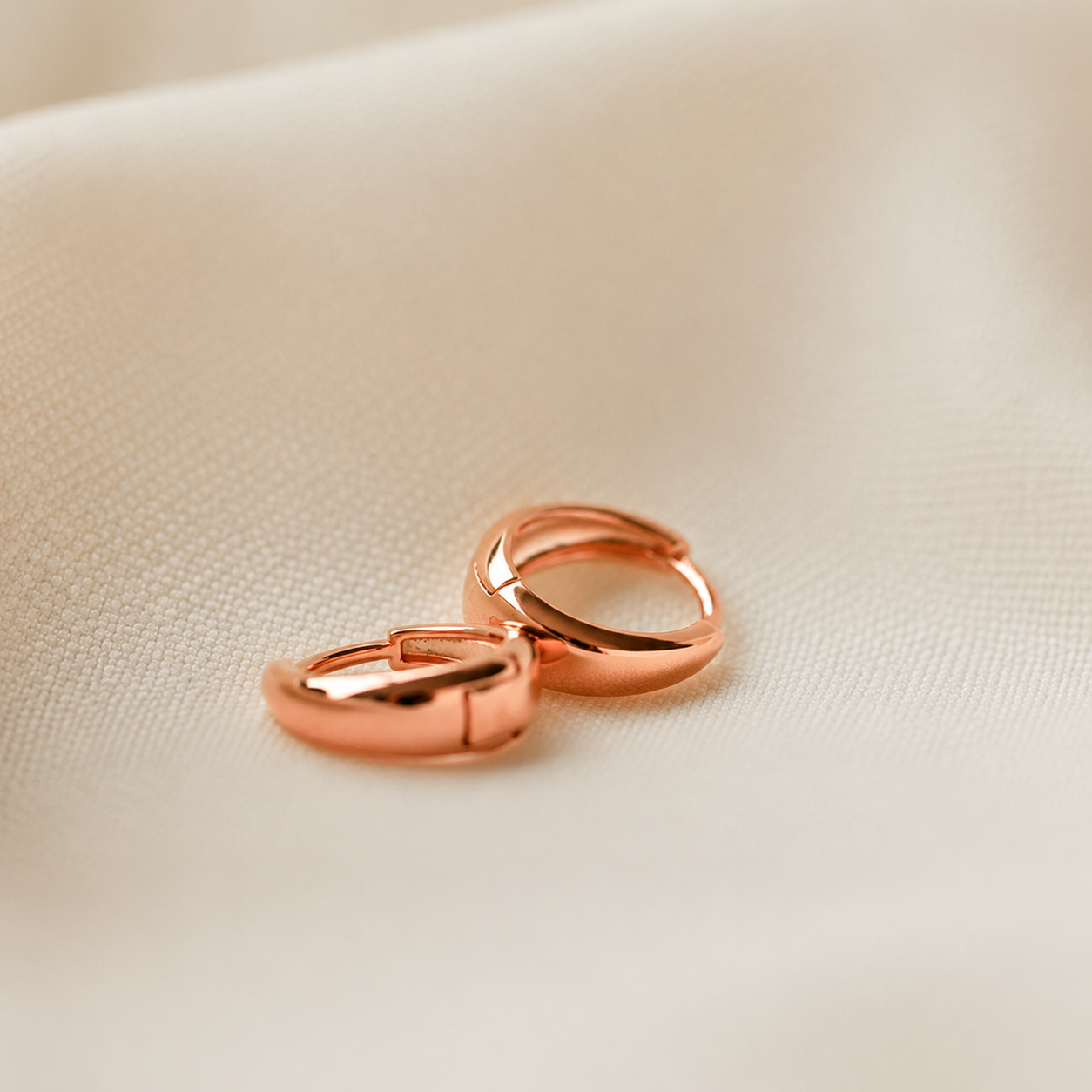 Rose gold hoop earrings on a beige fabric background